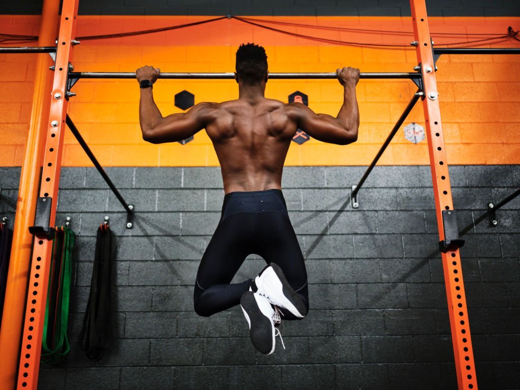 Man working out in a gym doing pull-ups on a bar.